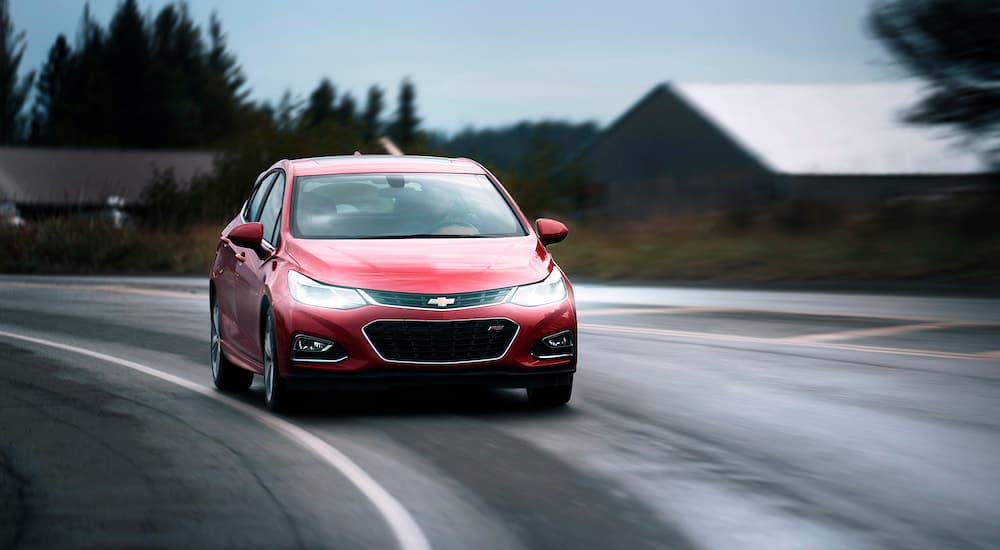 A red 2018 Chevy Cruze Hatchback Diesel is shown driving on a wet road after leaving a used car lot.