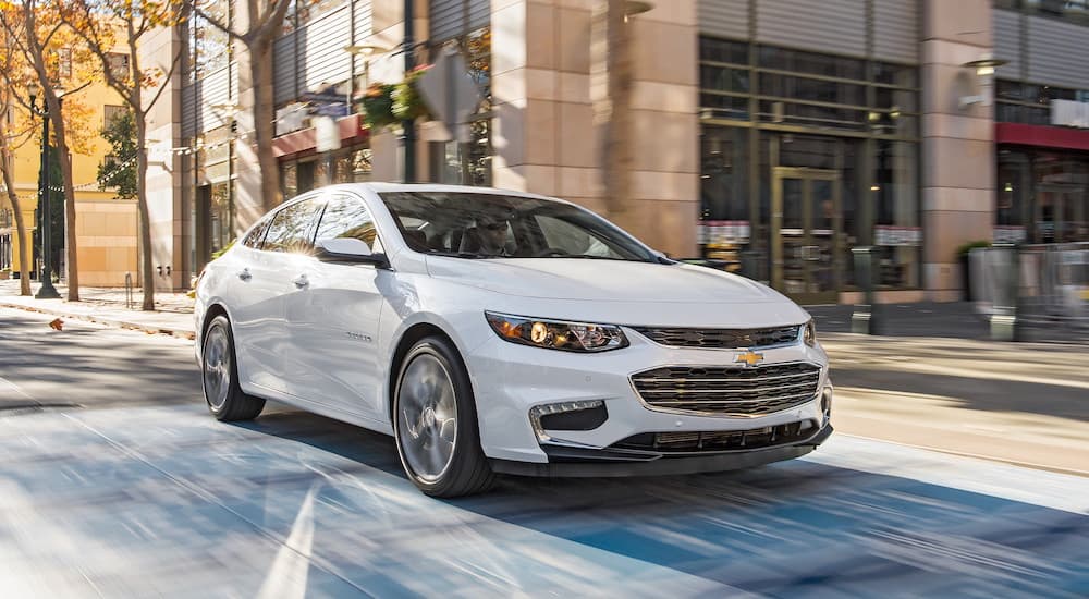 A white 2018 Chevy Malibu is shown driving on a city street.
