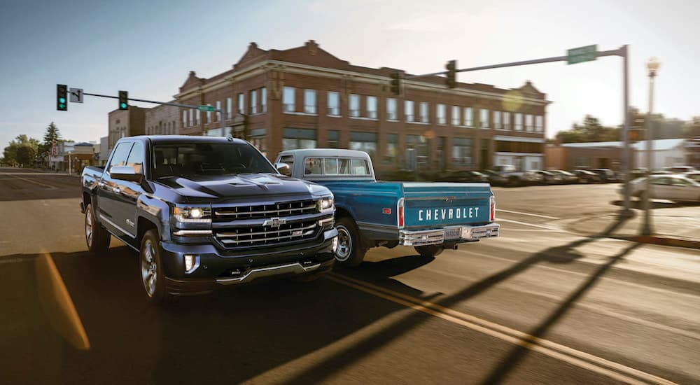 A dark blue 2018 Chevy Silverado 1500 Z71 Centennial Edition is shown driving past a light blue 1972 C10 after visiting a used truck dealer.