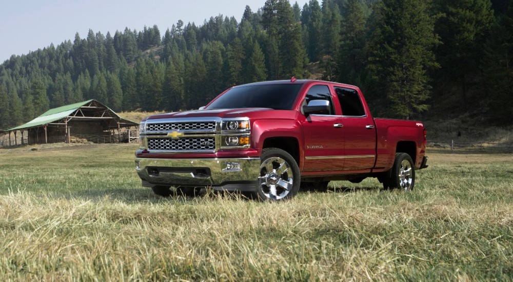 A red 2015 Chevy Silverado 1500 is shown parked in a field with a barn in the distance.